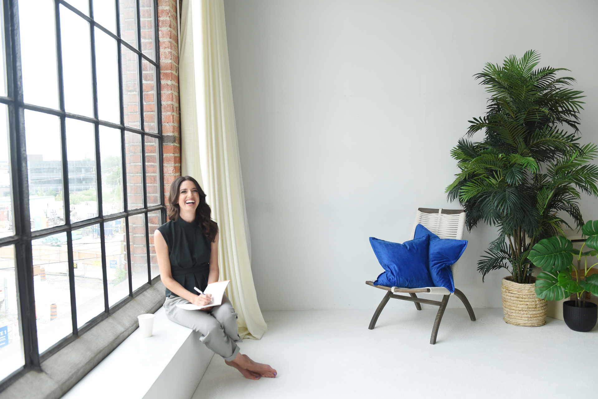 Fiona Stevenson laughing while journaling by a tall industrial window
